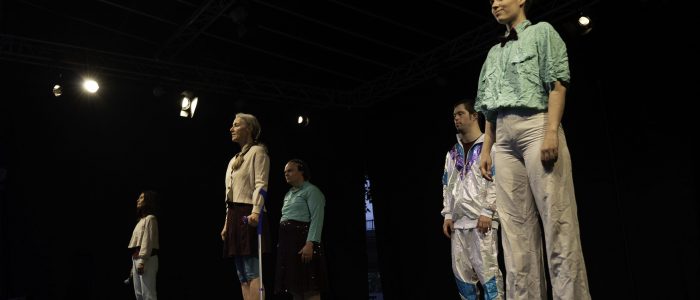 Alle fünf Performer*innen stehen gleichmäßig verteilt auf der Bühne der Night of Dance, vom Bühnenlicht hell erleuchtet und blicken ins Publikum.