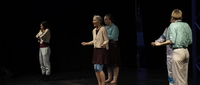 Die fünf Performer*innen stehen auf ihren Positionen auf der Bühne, die Hände zu Fäusten geballt, die Münder weit geöffnet zu einem imaginären Schrei. Sarahs Krücken liegen am Boden.